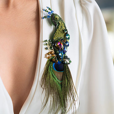 женщина держит в руках изящную брошь в виде павлина